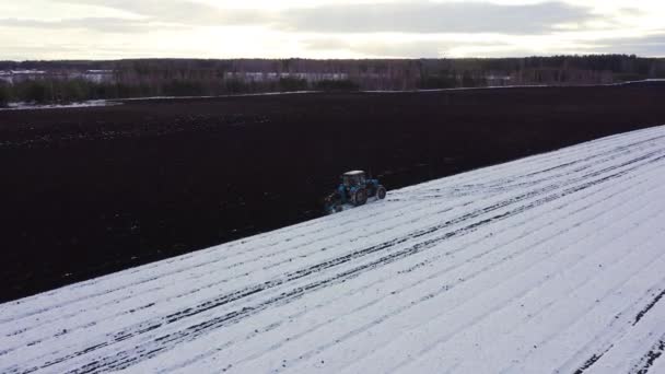 Un tractor azul arada un campo cubierto de nieve. Detrás del tractor hay tierra negra. Rusia, Ural. 4K — Vídeo de stock