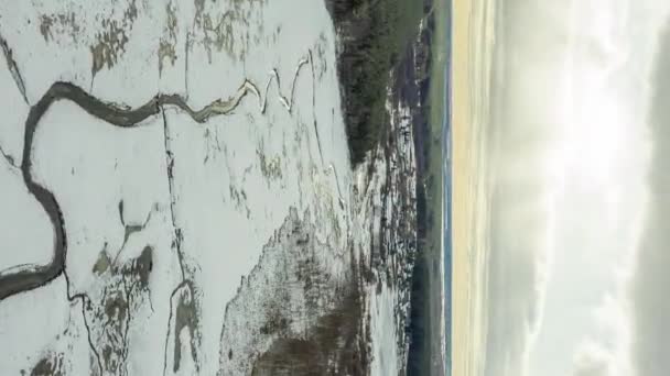 Πετώντας πάνω από ένα βάλτο καλυμμένο με χιόνι με μια σκοτεινή γραμμή του ποταμού. Το χωριό στο βάθος. Τα φώτα του ήλιου. 4K — Αρχείο Βίντεο