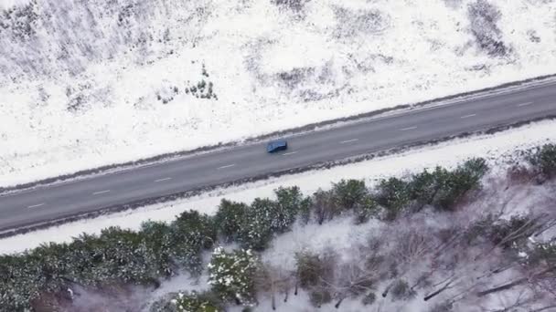 Niebieski samochód jedzie zimową asfaltową drogą. Droga biegnie wzdłuż linii energetycznych. Śnieg na drzewach i poboczach dróg. 4K — Wideo stockowe