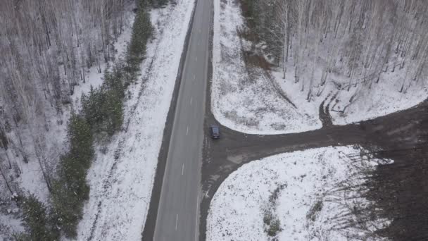 Niebieski samochód jedzie zimową asfaltową drogą w lesie. Śnieg na drzewach i poboczach dróg. 4K — Wideo stockowe
