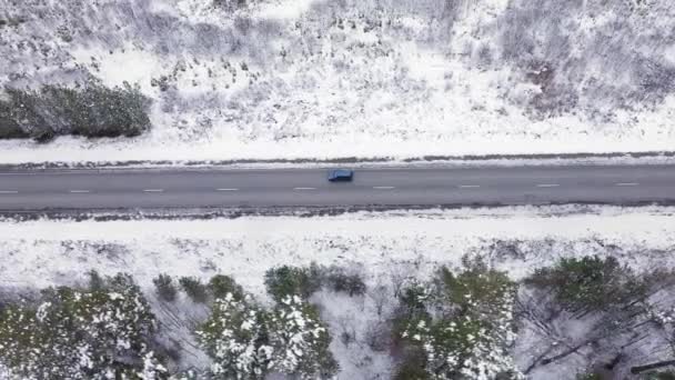 Un coche azul está conduciendo a lo largo de una carretera de asfalto de invierno. El camino va a lo largo de las líneas eléctricas. Nieve en árboles y bordes de carreteras. 4K — Vídeo de stock