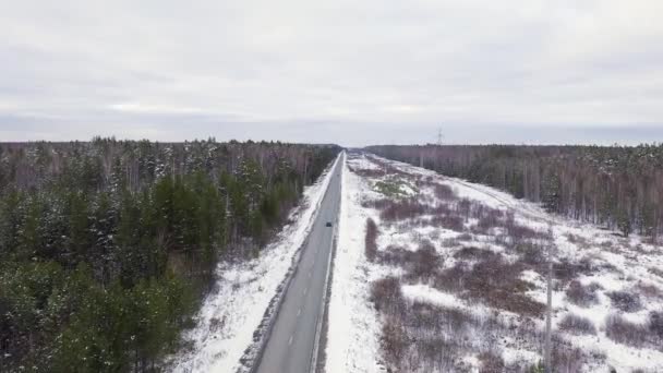 Een blauwe auto rijdt langs een winterasfaltweg. De weg loopt langs de hoogspanningsleidingen. Sneeuw op bomen en wegen. 4K — Stockvideo