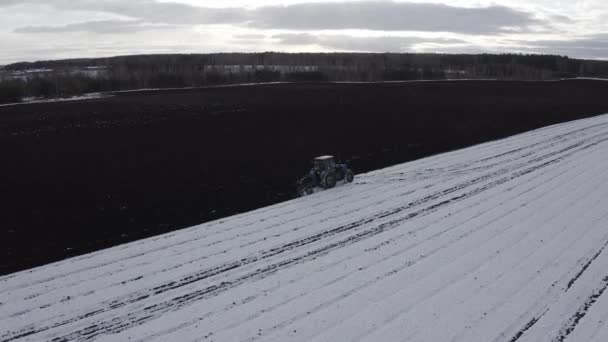 Un tractor azul arada un campo cubierto de nieve. Detrás del tractor hay tierra negra. Rusia, Ural. 4K — Vídeos de Stock