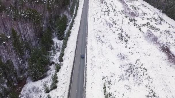 Ein blaues Auto fährt auf einer winterlichen Asphaltstraße. Die Straße verläuft entlang der Stromleitungen. Schnee an Bäumen und Straßenrändern. 4K — Stockvideo