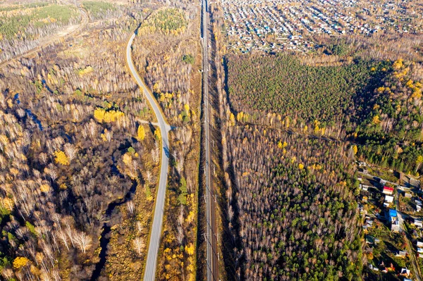 The road runs parallel to the railway. Holiday villages. Flying over the autumn mixed forest during sunset. Ural, Russia