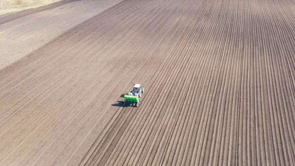 Russia, the Urals. Planting potatoes on the field with a combine and tractor. Spring, Aerial View