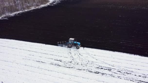 Un tractor azul arada un campo cubierto de nieve. Detrás del tractor hay tierra negra. Rusia, Ural. 4K — Vídeo de stock