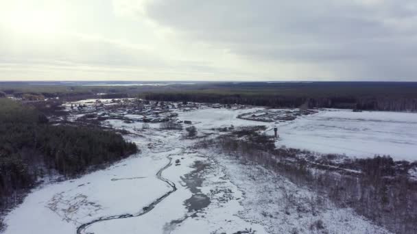 Заводские угодья с небольшой рекой, покрытой снегом. Деревня на заднем плане. Облака и солнце. Снег на деревьях. 4K — стоковое видео