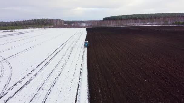 Un tractor azul arada un campo cubierto de nieve. Detrás del tractor hay tierra negra. Rusia, Ural. 4K — Vídeo de stock