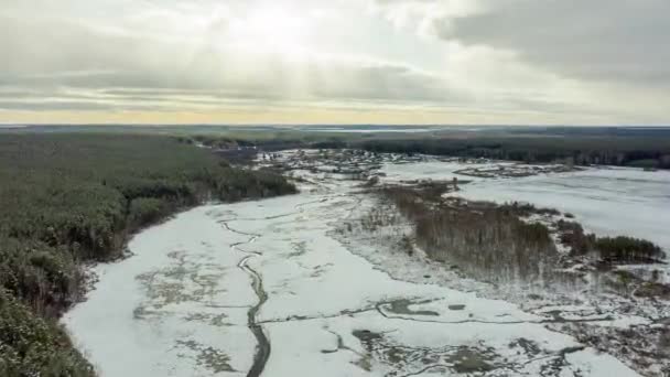 川の暗いストリークで雪で覆われた沼を飛んでいます。背景にある村。太陽の光。4K — ストック動画