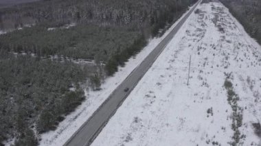 Mavi bir araba kış asfalt yolu boyunca gidiyor. Yol elektrik hatları boyunca uzanıyor. Ağaçlarda ve yol kenarlarında kar. 4K