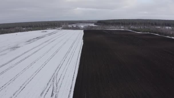 Een blauwe trekker ploegt een veld bedekt met sneeuw. Achter de trekker is zwarte aarde. Rusland, Oeral. 4K — Stockvideo