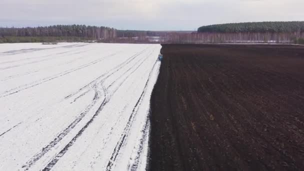 Dolly zoom. Un tractor azul arada un campo cubierto de nieve. Detrás del tractor hay tierra negra. Rusia, Ural — Vídeo de stock