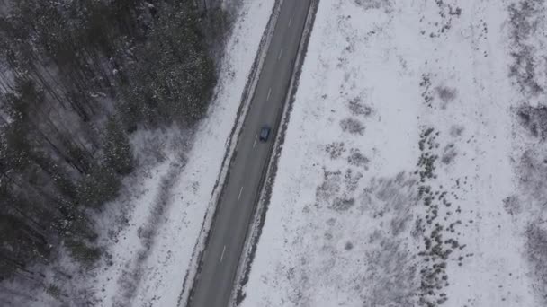 Een blauwe auto rijdt langs een winterasfaltweg. De weg loopt langs de hoogspanningsleidingen. Sneeuw op bomen en wegen. 4K — Stockvideo