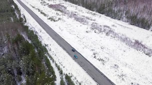 Een blauwe auto rijdt langs een winterasfaltweg. De weg loopt langs de hoogspanningsleidingen. Sneeuw op bomen en wegen. 4K — Stockvideo
