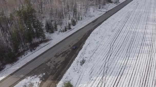 Blauwe auto rijdt op de weg. Rond het veld en het bos zijn bedekt met sneeuw. Rusland, Oeral. 4K — Stockvideo