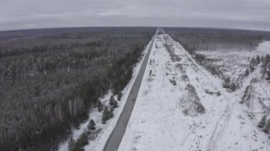 Mavi bir araba kış asfalt yolu boyunca gidiyor. Yol elektrik hatları boyunca uzanıyor. Ağaçlarda ve yol kenarlarında kar. 4K