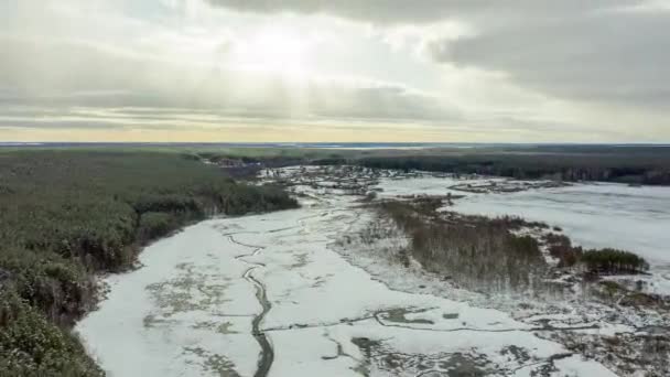 川の暗いストリークで雪で覆われた沼を飛んでいます。背景にある村。太陽の光。4K — ストック動画