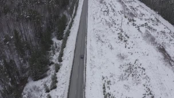 Um carro azul está dirigindo ao longo de uma estrada de asfalto de inverno. A estrada vai ao longo das linhas de energia. Neve nas árvores e nas estradas. 4K — Vídeo de Stock