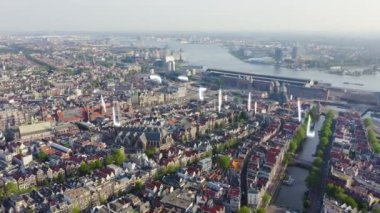 Amsterdam, Hollanda. Amsterdam Merkez İstasyonu (Amsterdam Centraal) ve Oudekerk Kilisesi (De Oude Kerk) çevresindeki çatıların üzerinden uçuyor. 4K