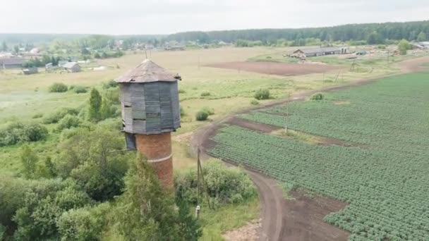 Rusya, Ural. Tarlaların üzerinde uçuyor. Patates yetiştirme sıraları. Eski kırmızı tuğlalı su kulesi. 4K — Stok video