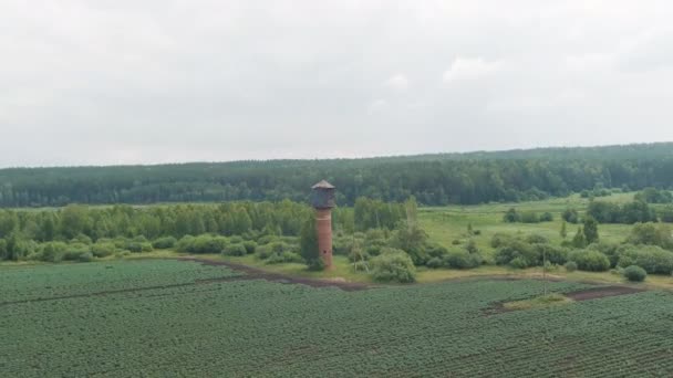 Rusia, Ural. Zboară peste câmpuri. Rânduri de cartofi în creștere. Turnul vechi de apă din cărămidă roşie. 4K — Videoclip de stoc