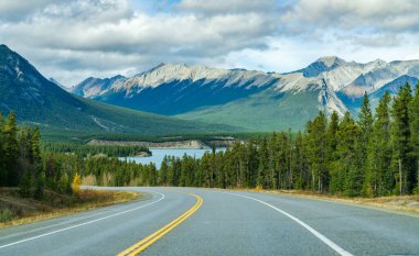Rural road in the forest with mountains in the background. Alberta Highway 11 (David Thompson Hwy) along the Abraham lake shore. Jasper National Park, Canada. clipart