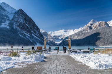 Alberta, Kanada - OCT 10 2020: Fairmont Chateau Lake Louise, güneşli bir kış sabahı. Turkuaz renkli su yüzeyinde süzülen sis. Açık mavi gökyüzü, arka planda karlı dağlar.