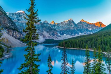 Moraine Gölü 'nün güneşli yaz gününde gün doğumu. Ten Peaks 'in karla kaplı vadisi kırmızıya dönüyor ve turkuaz renkli su yüzeyine yansıyor. Banff Ulusal Parkı 'ndaki manzara, Alberta, Kanada.