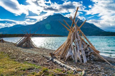 Driftwood Sahili, Middle Waterton Gölü göl kıyısı sonbahar yaprakları mevsimi sabahı. Mavi gökyüzü, arkadaki dağların üzerinden beyaz bulutlar. Waterton Lakes Ulusal Parkı, Alberta, Kanada.