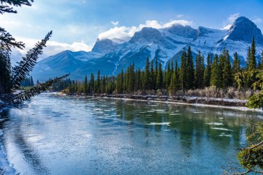 Kış mevsiminin erken saatlerinde doğal manzara güneşli bir sabah. Bow River 'da yüzen buz tabakası. Açık mavi gökyüzü, arka planda Lawrence Grassi Dağı karla kaplı. Canmore, Alberta, Kanada 'da manzara.