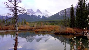 Kar, Üç Kız Kardeş üçlüsünün zirvesini mavi gökyüzü ile kapladı ve sonbaharda beyaz bulutlar su yüzeyine yansıdı. Canmore, Canadian Rockies, Alberta, Kanada 'daki güzel doğal manzara.