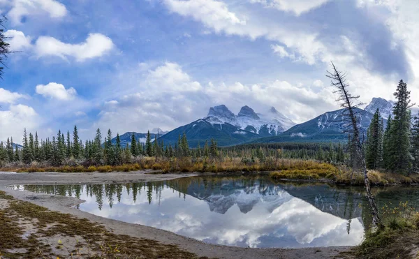 Снег покрыл трио "Три сестры" вершины горы с голубым небом и белыми облаками, отражающимися на поверхности воды осенью. Красивый природный пейзаж в Канморе, Канадские Скалистые горы, Альберта, Канада. — стоковое фото