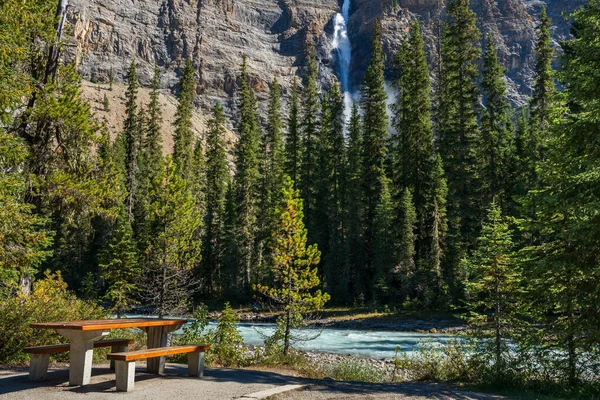 Wooden bench by the Yoho River over Takakkaw Falls Waterfall in a sunny summer day. Yoho National Park, Canadian Rockies, British Columbia, Canada. — Stock Photo, Image