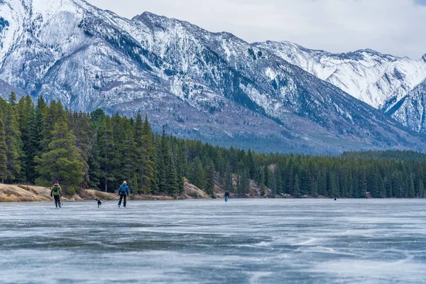 Туристы катаются на коньках в озере Джонсон зимой. Заснеженная гора на заднем плане. Национальный парк Банф, Канадские Скалистые горы, Альберта, Канада. — стоковое фото