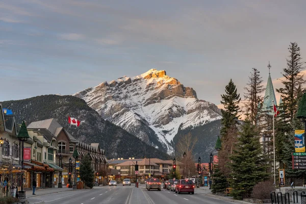 Banff, Alberta, Kanada - 1. NOV 2020: Straßenansicht der Banff Avenue am Herbstabend. Schneebedeckte Cascade Mountain mit rosa Himmel im Hintergrund. — Stockfoto