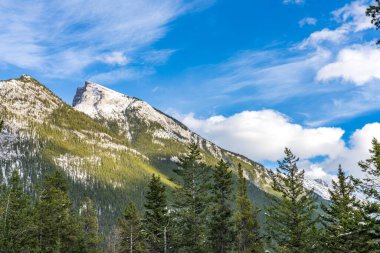Karla kaplı Rundle Dağı sıradağları. Mavi gökyüzü üzerinde karlı orman ve kışın güneşli bir günde beyaz bulutlar. Banff Ulusal Parkı, Kanada Kayalıkları.