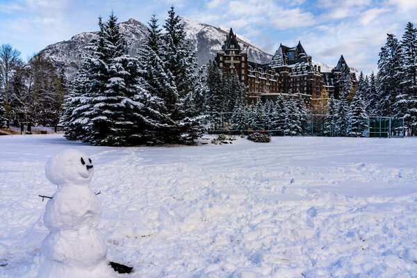 A smiling snowman in the snowy playground. Fairmont Banff Springs in the background. Banff National Park, Canadian Rockies.