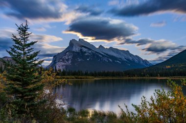 Yaz gecesi Vermilion Gölünde ayın doğuşu. Banff Ulusal Parkı, Canadian Rockies, Alberta, Kanada. Rundle Dağı 'nın üzerindeki parlak dolunay ve göl yüzeyindeki altın yansıma ile geceyi aydınlatıyor..