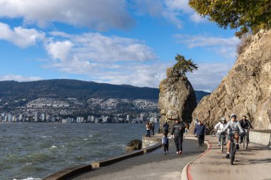 Vancouver, BC, Kanada - MAR 16 2021: Güneşli bir günde Stanley Park Seawall Siwash Rock 'ta insanlar bisiklet sürüyor.