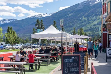 Jasper, Alberta, Kanada - 17 Haziran 2021: Covid-19 salgın döneminde yaz aylarında Jasper Kasabası sokak manzarası. İnsanlar kaldırımda oturuyor, restoranların dışında yemek yiyorlar..