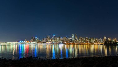 Vancouver şehir merkezi gökyüzü gece panoraması. Renkli binalar liman su yüzeyine yansıyor. British Columbia, Kanada.