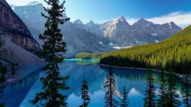 Moraine Gölü 'nde sabahtan öğlene kadar güneşli yaz günlerinde. Gölge yüzeyde hareket eder ve On Tepe Vadisi 'nin karla kaplı yansıması turkuaz renkli su üzerinde. Banff Ulusal Parkı, Alberta, Kanada.