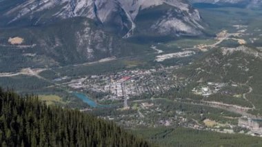 Yaz mevsiminde güneşli bir günde çevresindeki dağlarla Banff kasabası. Sülfür Dağı 'nın zirve gözlem güvertesinden görüntü. Alberta, Kanada. Uzaklara yakınlaşmak üzereyken hızlandırılmış 4K UHD.