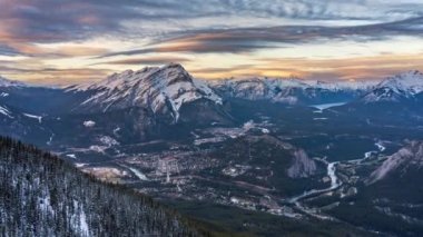 Banff kasabasının kar mevsiminde gün batımı manzarası. Renkli bulutlar, Şelale Dağı ve alacakaranlıkta çevresindeki dağlar. Banff Ulusal Parkı, Alberta, Kanada. 4K Zaman atlamalı yakınlaştır.