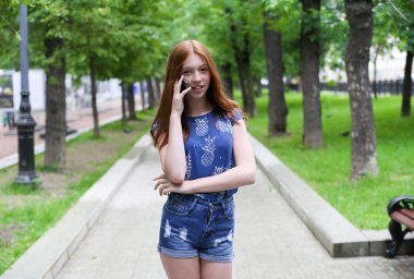  Güzel ve ince kız parkta ve telefonda konuşurken mevcuttur. Mutlu kadın. 