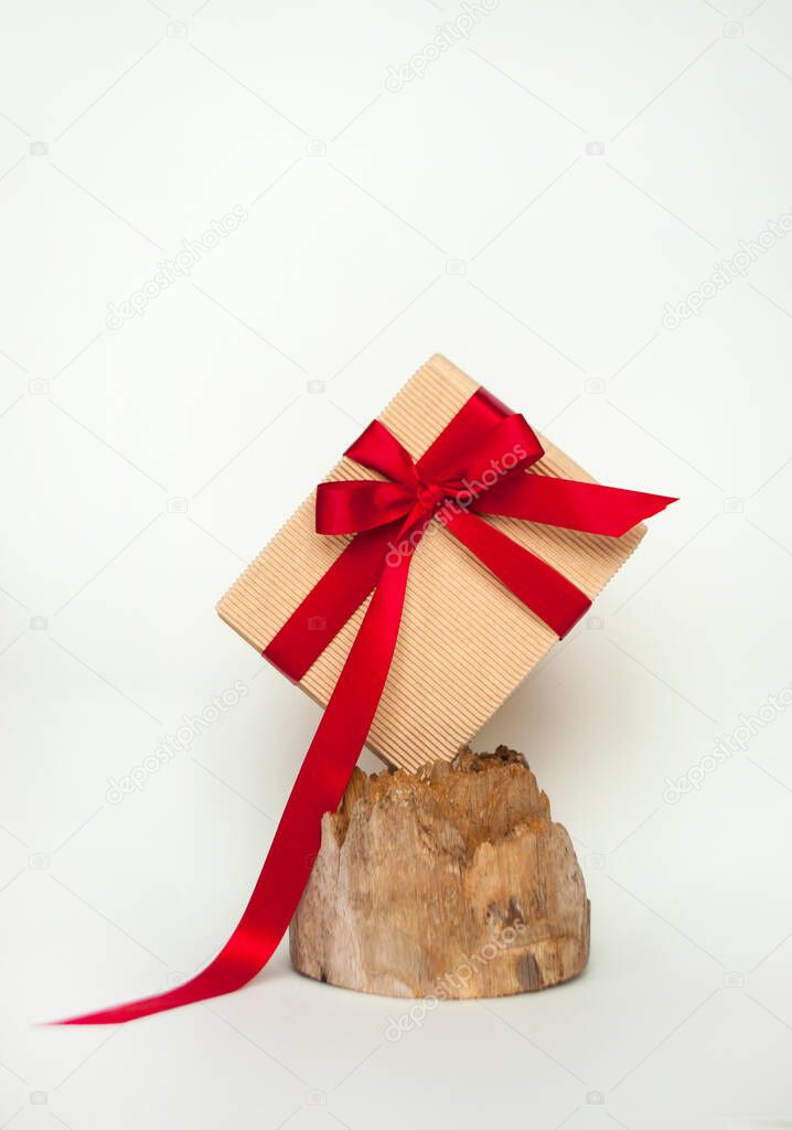 Giftbox wrapped in craft paper bowed with red ribbon on a beautiful wooden stump.