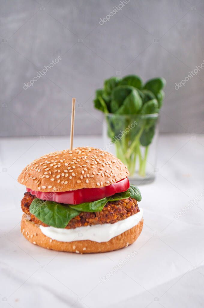 Vegan burger made with red beans, red pepper, spinach, white yoghurt and fresh salad leaves and cut vegetables at the background.