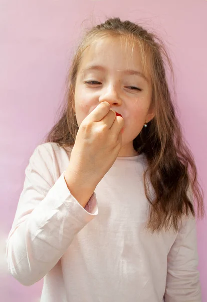 Uma menina feliz está comendo um suculento morango doce em um fundo rosa. — Fotografia de Stock