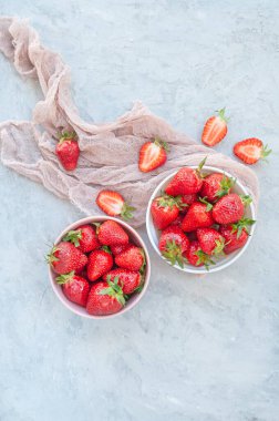 Taze olgun çilekler bembeyaz ve pembe kâselerde gri arka planda yatıyordu..